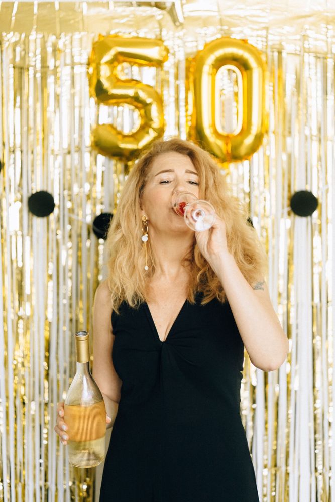 Woman drinking champagne in front of 50 balloons celebrating healthy aging