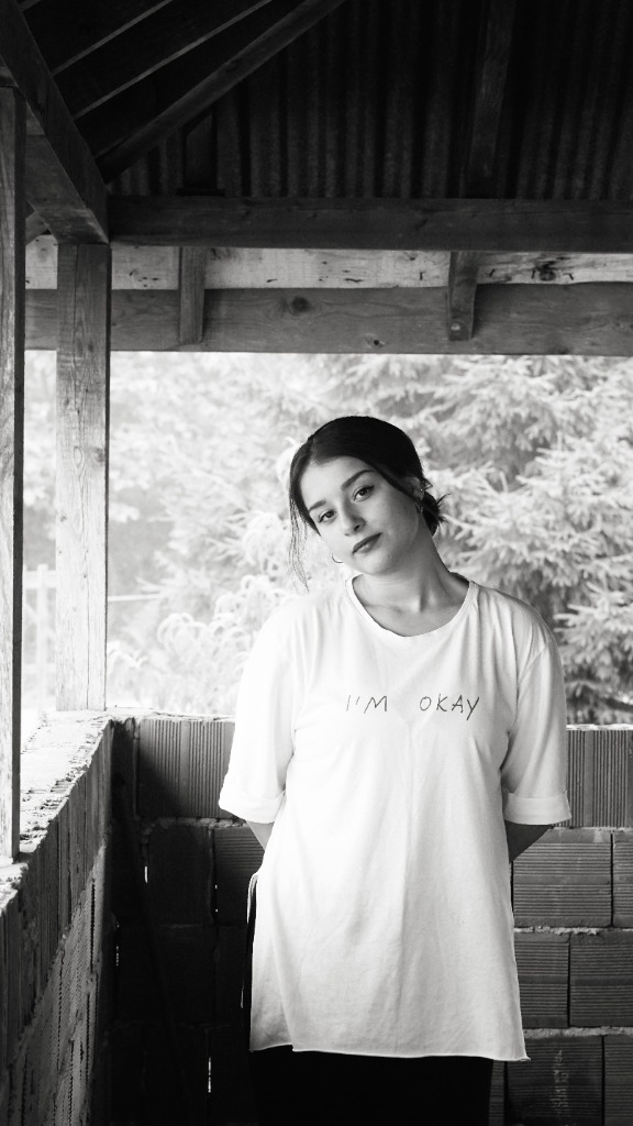 A young woman looking thoughtfully at the camera, wearing a t-shirt that reads 'I'm okay'