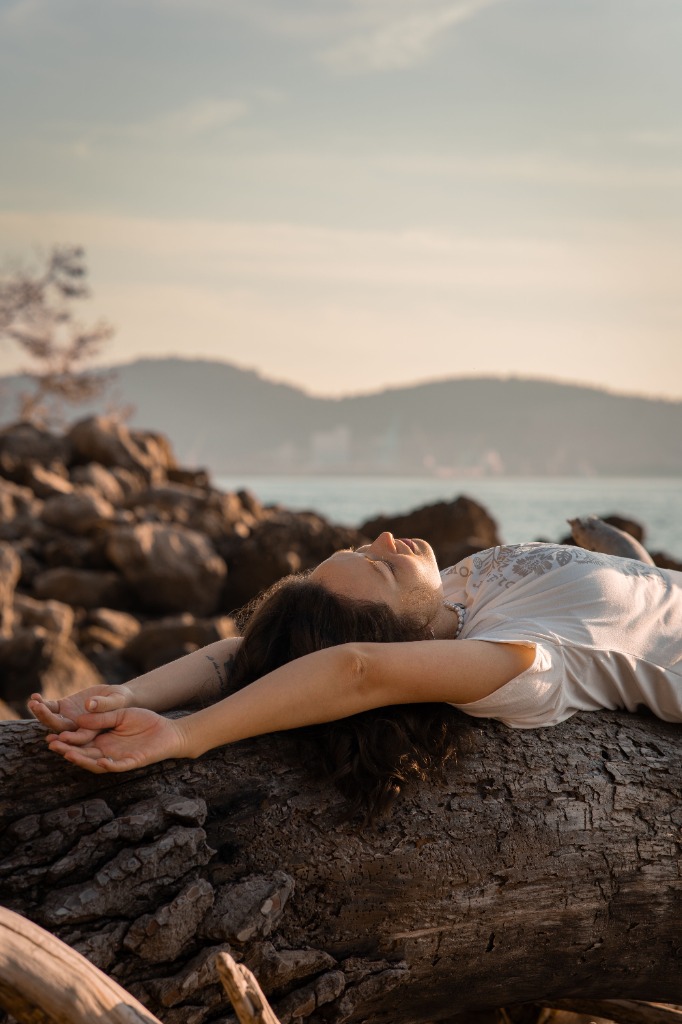 A woman sleeping comfortably on a log near the ocean during sunset